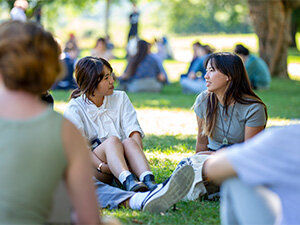 two college students chatting and sitting on the grass