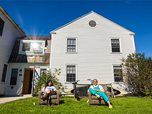 house with students sitting on lawn chairs in front of a blue sky