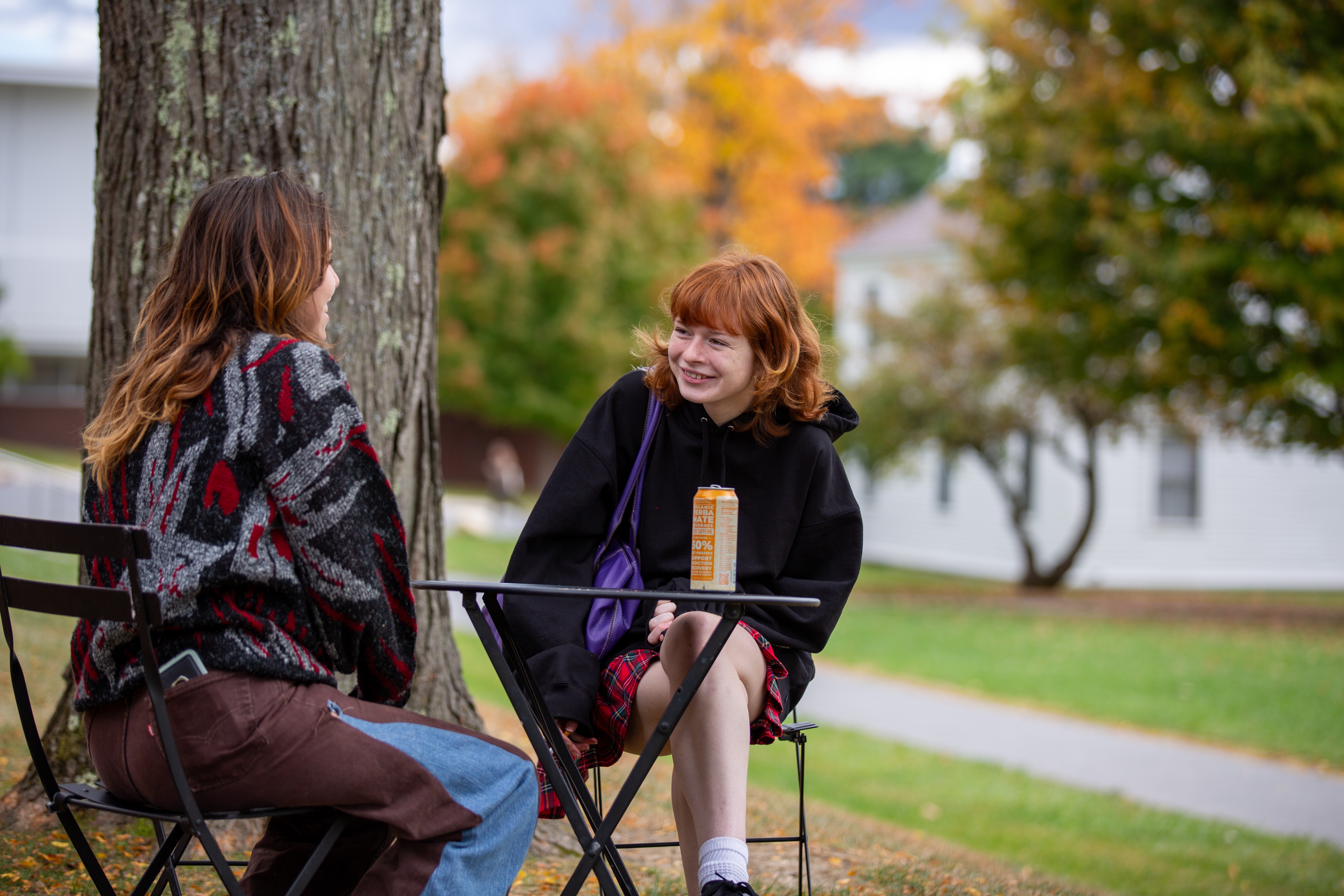 two students outside talking under a tree