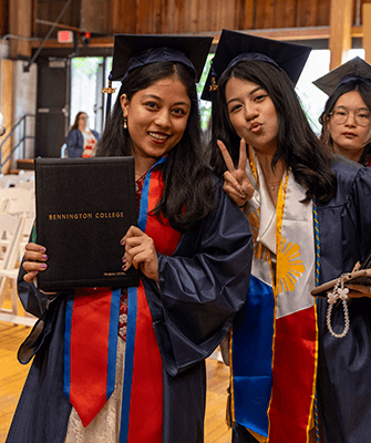 two Bennington graduates pose during commencement wearing their regalia