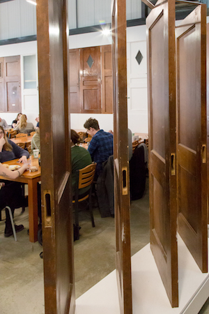 four wooden doors mounted standing upright for display, with students dining in background