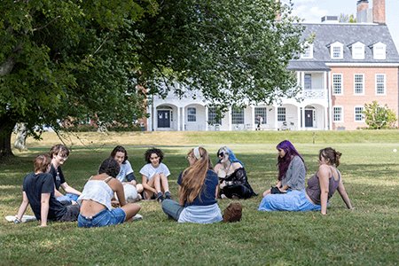 students sit outside on the lawn in a circle