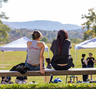 two students look out at the mountains while sitting on a railing