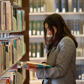 a student holding a book standing in the middle of library bookshelves