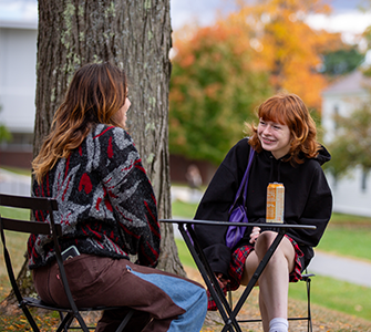 Two students are engaged in conversation while sitting outside at a small table