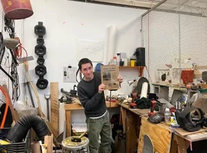 Image of Cyrus Vella '26 in his studio, posing with the poster for his creek-clearing project.