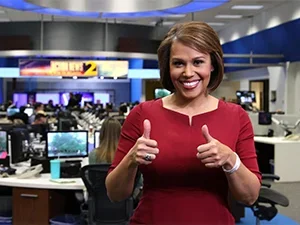 Jovita in the newsroom giving a thumbs-up to the camera 