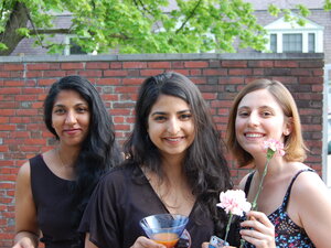 three students in a garden in fancy dress hold cocktails and smile at the camera
