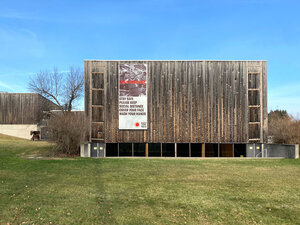 Wood Sided building (VAPA) with a large banner hanging on the wall, green grass, blue sky