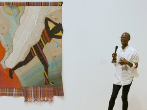 man with microphone standing near giant tapestry 