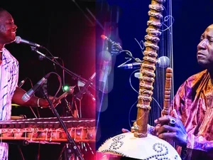 Two men in colorful lighting and colorful clothes playing a balafon and a kora