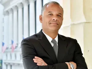 A bald man in a suit with his arms crossed