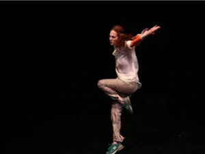 Woman with red hair dressed in white jumping in front of a black background