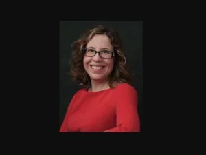 A woman (Stiliana Milkova) with dark hair wearing glasses smiles