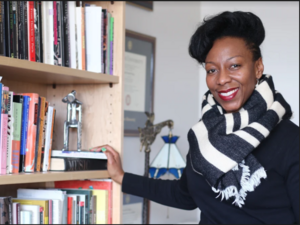 smiling woman in striped scarf beside a bookshelf