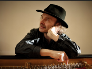 man in a hat leans over an open piano
