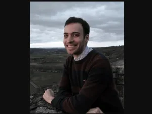 smiling man in a sweater above a bleak landscape