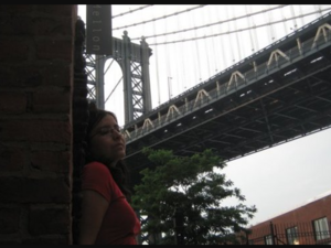 woman in red leans against a wall under a bridge