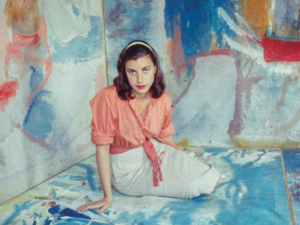Helen Frankenthaler sitting in front of colourful canvas