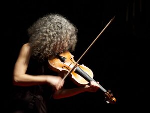 Woman with grey hair in profile playing violin in black background