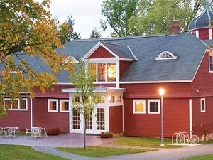 A red barn with a tree in the front, a table and chairs, and lights around the perimeter