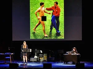 Live recording of Criminal Podcast. Woman with microphone on stage in front of a projection.