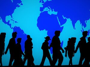 Black figures walking in front of a blue wall featuring the map of the world