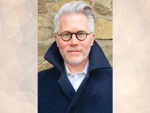 man with white hair and glasses wearing a black coat. 