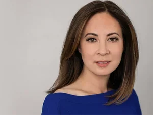 Paisley Rekdal, with dark smooth hair and a blue dress, stares at the camera 