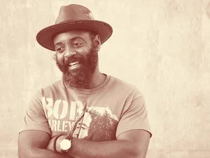Reginald Dwayne Betts stands with arms crossed wearing a hat