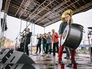 A band on an outdoor stage with drums, trombones, and accordions