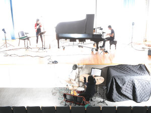 faded photo of a trio, piano, flute, drum set, in bright sunlight on a stage