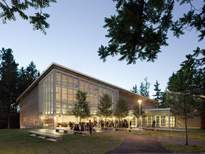 dusk and the lit student center building with glass windows and inky trees in the foreground