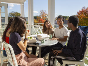 students eating on the balcony, with a tree with fall foliage in the background