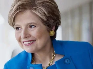 Woman with short blonde hair and blue suit smiling, with white background