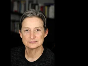 Woman with short grey hair and black shirt stares directly at camera