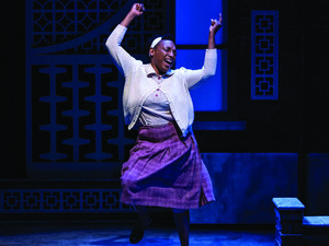 Woman dancing with joy on stage wearing a white sweater and purple skirt, blue lighting