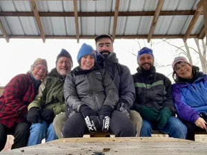 a small group of alumns pose for a photo in winter beneath a small shelter