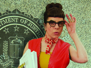 Liz, wearing a red dress, in front of the Department of Justice, holding her play