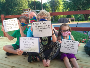 Image of family wearing masks and holding signs
