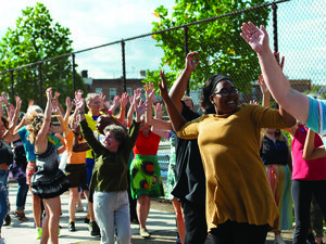 a group of dancers perform outside, they are raising their arms and wearing bright colors