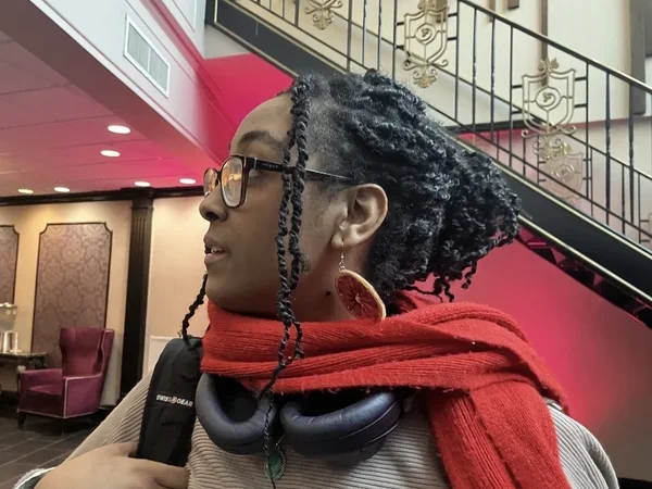 Blu Mehari '26 in right-facing profile wearing headphones and a red scarf around her neck and carrying a bag on her right shoulder