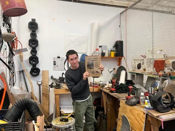 Image of Cyrus Vella '26 in his studio, posing with the poster for his creek-clearing project.