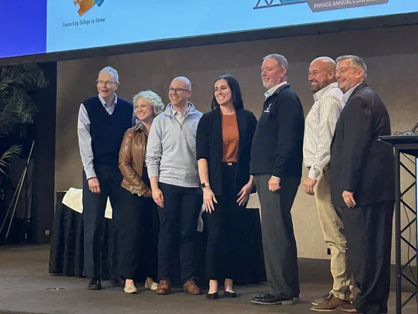 A group of seven smiling people on a stage