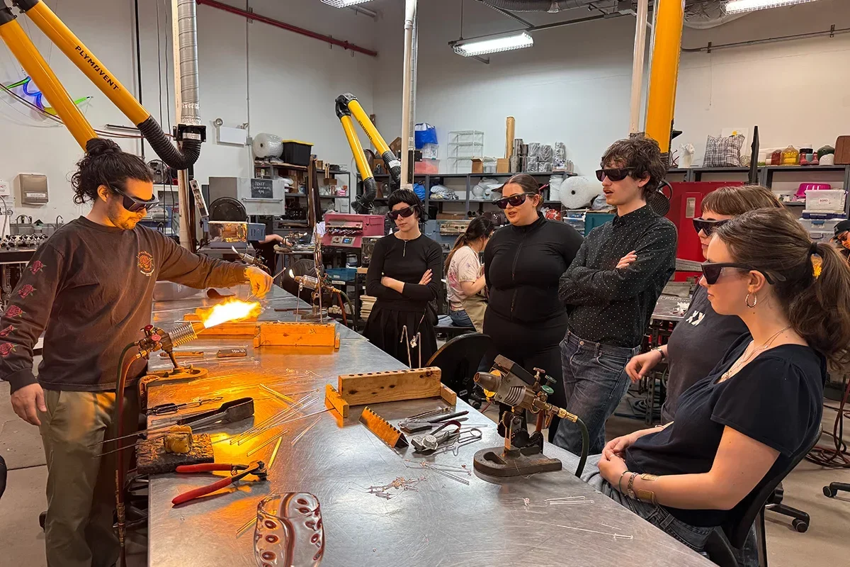 Image of River Valadez ’20 (MFT ’19) leads Fellows in a flameworking class at Urban Glass.