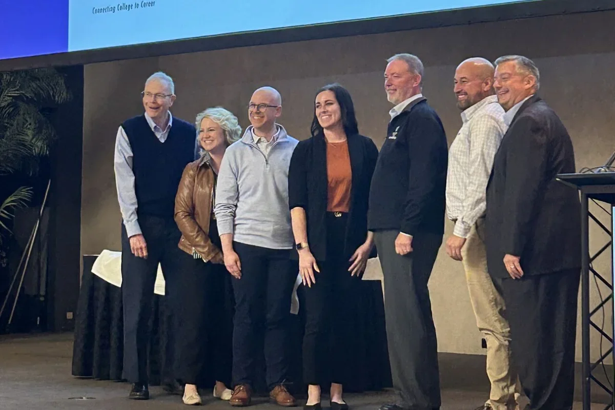 A group of seven smiling people on a stage