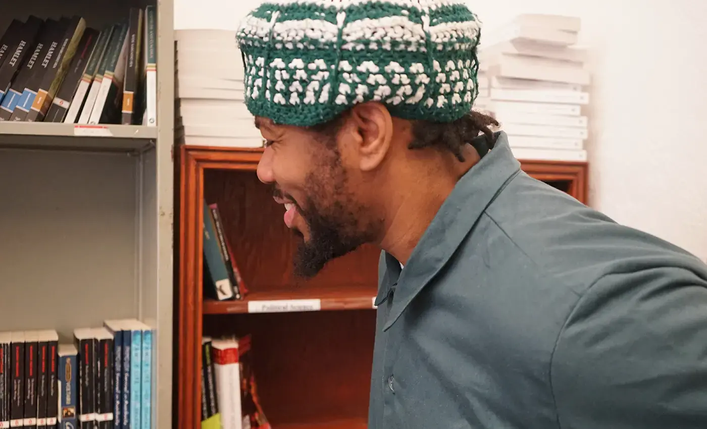 PEI student in green hat looking at bookshelf and smiling