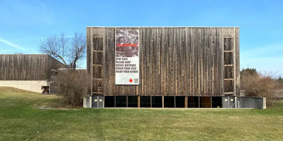 Wood Sided building (VAPA) with a large banner hanging on the wall, green grass, blue sky