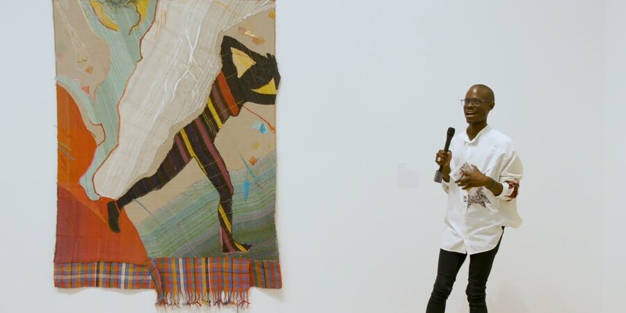 man with microphone standing near giant tapestry 