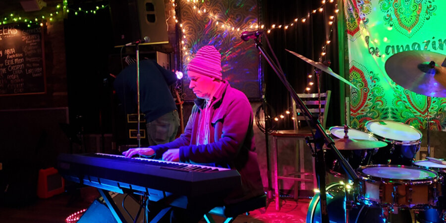Man with striped hat playing a keyboard piano under purple light